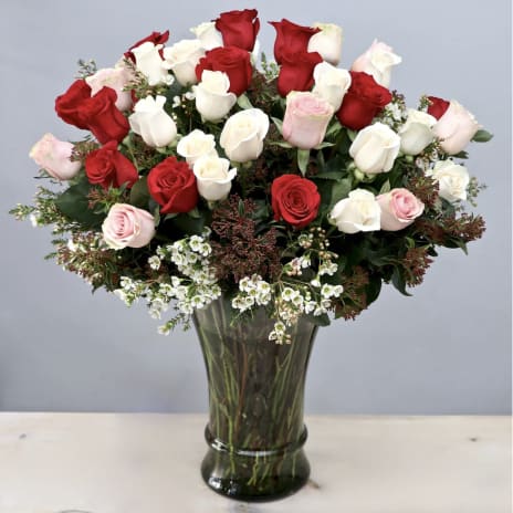 Tall vase of red, white, and pale pink roses with small white filler flowers.