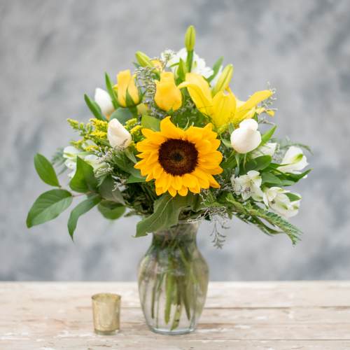 Sunflower and yellow rose bouquet in a glass vase with white blooms