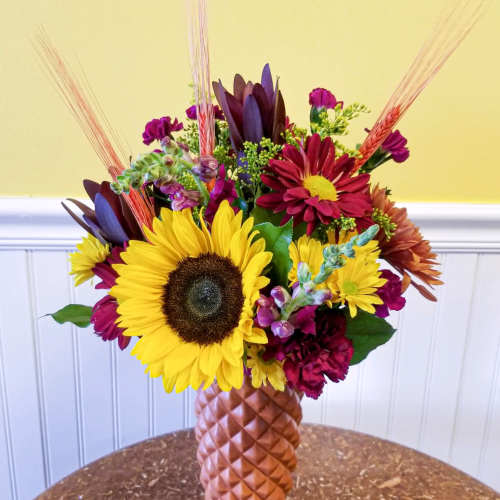 Mixed bouquet with sunflowers and burgundy blooms in a textured vase