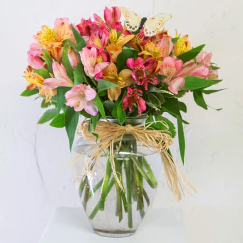 Mixed pink and yellow flowers in a glass vase with a butterfly pick
