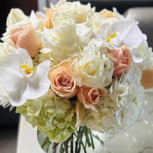 Bouquet of white and peach roses with white orchids in a glass vase