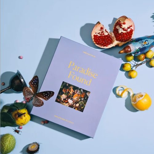 Paradise Found jigsaw puzzle box styled with colorful fruits, insects, and a metal goblet on a blue surface