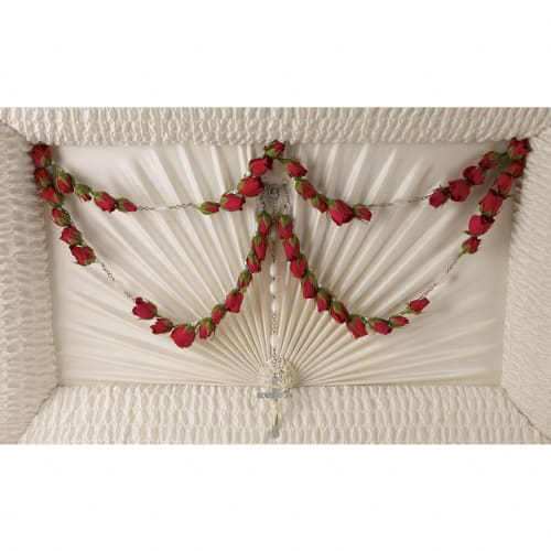 White coffin interior with red rose garlands and a rosary cross