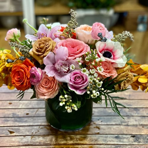Mixed bouquet of pink, peach, and orange flowers in a dark glass vase