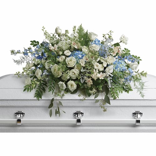 White and blue floral casket spray on a white casket