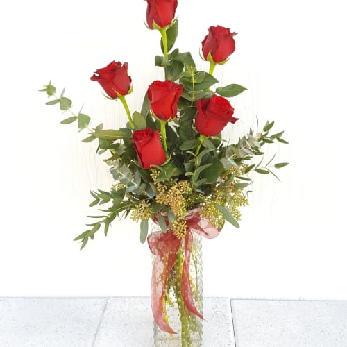 Tall bouquet of red roses in a clear glass vase with ribbon