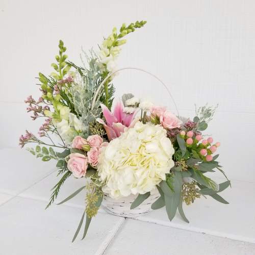 Basket arrangement with pink roses, white hydrangea, and tall white blooms