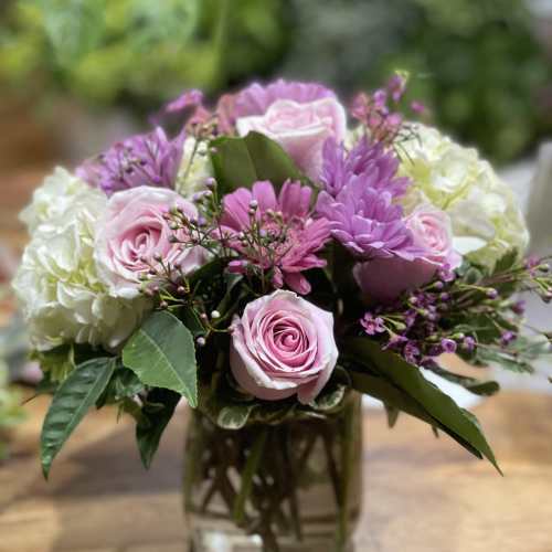 Pink roses and purple flowers arranged in a glass vase