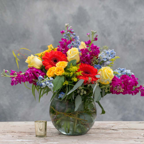 Mixed bouquet of roses, gerbera daisies, and purple blooms in a glass vase