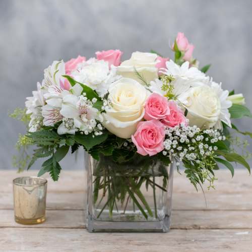 Pink and white roses arranged in a clear square vase