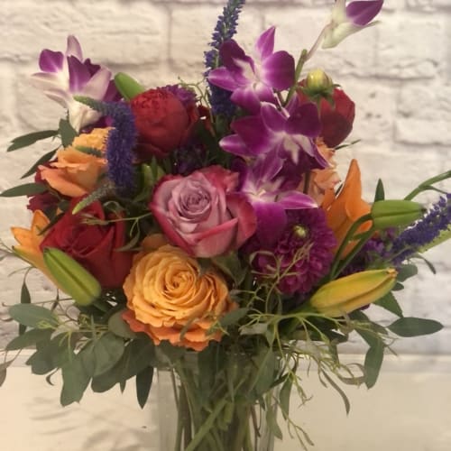 Mixed bouquet of roses, orchids, and lilies in a clear glass vase