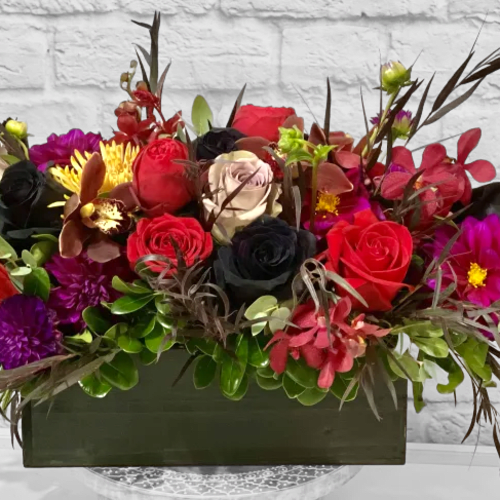 Rectangular floral arrangement with red, black, and purple blooms in a dark container