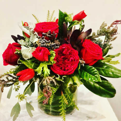 Red roses and mixed greenery arranged in a clear glass vase