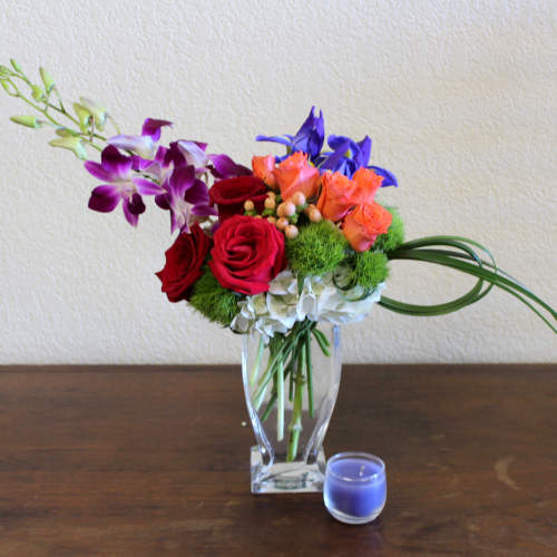 Mixed bouquet of roses and orchids in a clear glass vase with a small blue candle