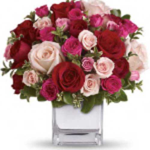 Round arrangement of red, hot pink, and pale pink roses in a clear glass cube vase