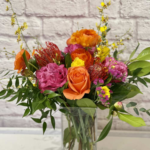 Mixed bouquet of orange, pink, and yellow flowers in a clear glass vase