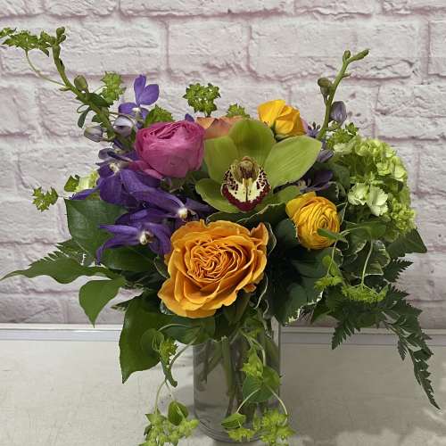 Mixed bouquet in a clear glass vase with orange, pink, purple, and green blooms