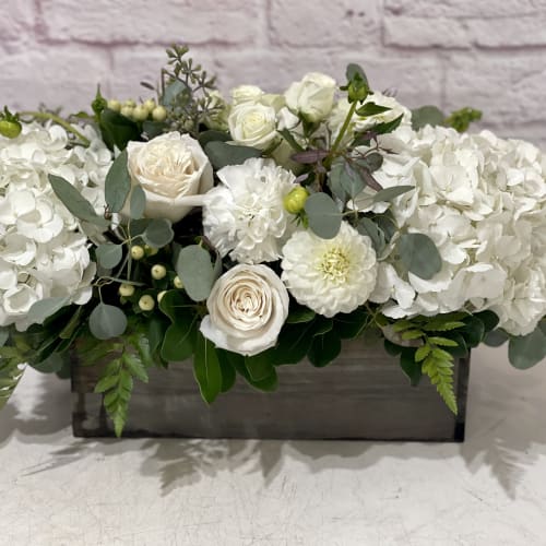 White floral arrangement in a rectangular wooden box with roses and hydrangeas