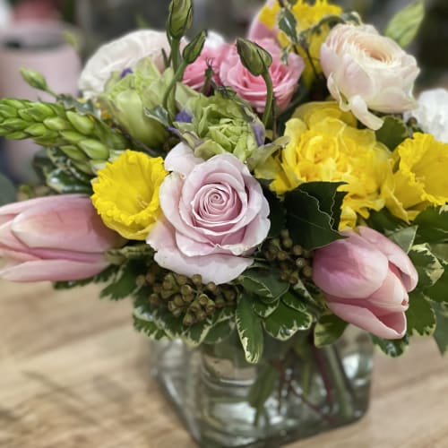 Mixed bouquet of pink roses, yellow blooms, and tulips in a glass vase
