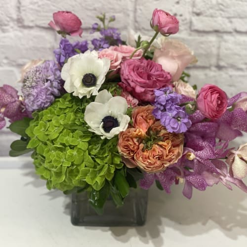 Mixed bouquet in a square glass vase with pink, purple, white, and green blooms