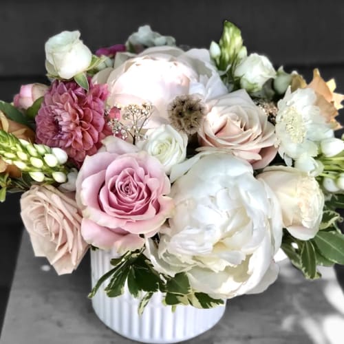 Low arrangement of white peonies, blush roses, and mixed blooms in a white ribbed ceramic vase