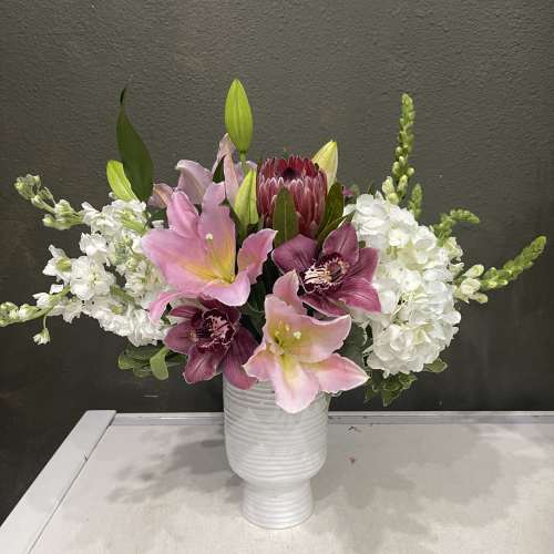 Pink lilies and white blooms arranged in a white vase