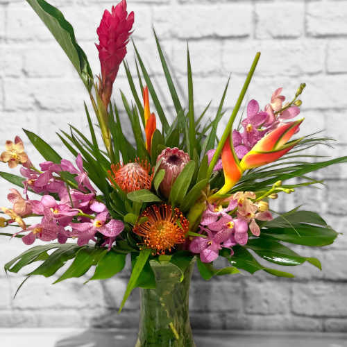 Tropical bouquet with orchids and orange blooms in a glass vase