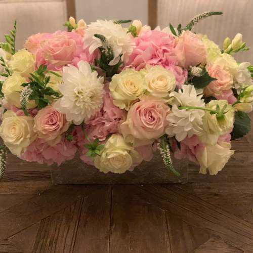 Low floral arrangement of pink and white roses in a clear rectangular vase
