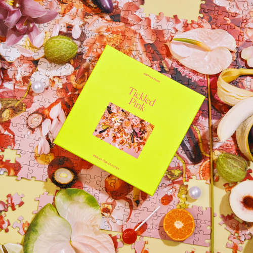 Bright yellow 'Tickled Pink' 500-piece puzzle box on a floral puzzle with scattered fruits and flowers