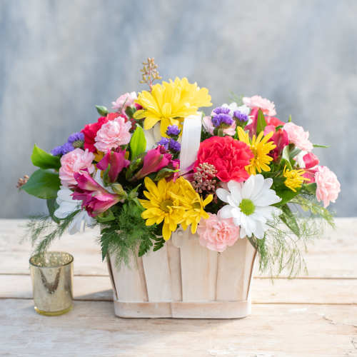 Mixed bouquet in a wooden basket with pink, yellow, white, and purple flowers