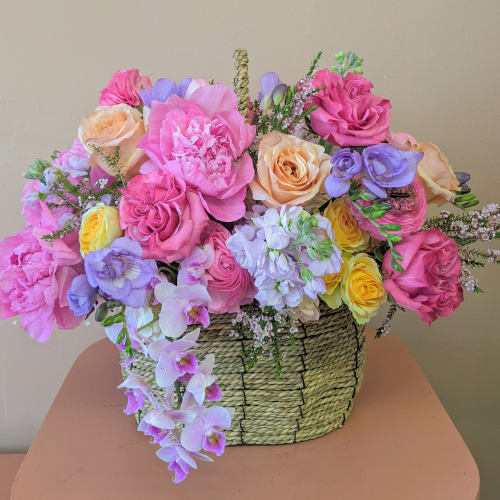 Mixed pink, peach, yellow, and lavender flowers in a woven basket