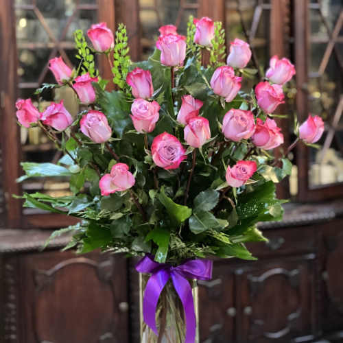Pink roses arranged in a clear glass vase with a purple ribbon