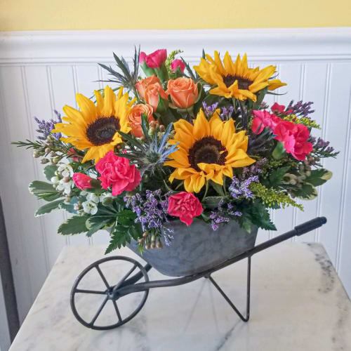 Sunflowers, roses, and carnations arranged in a wheelbarrow planter