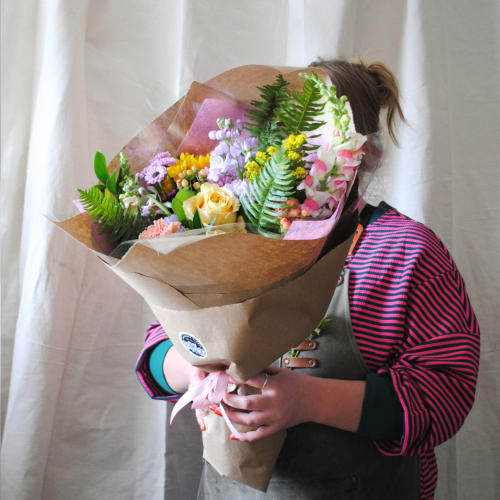 Person holding a mixed bouquet wrapped in brown paper and pink tissue