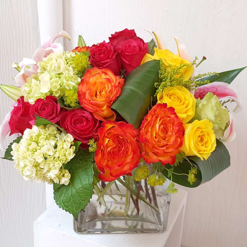 Mixed bouquet of roses, hydrangeas, and lilies in a clear glass vase