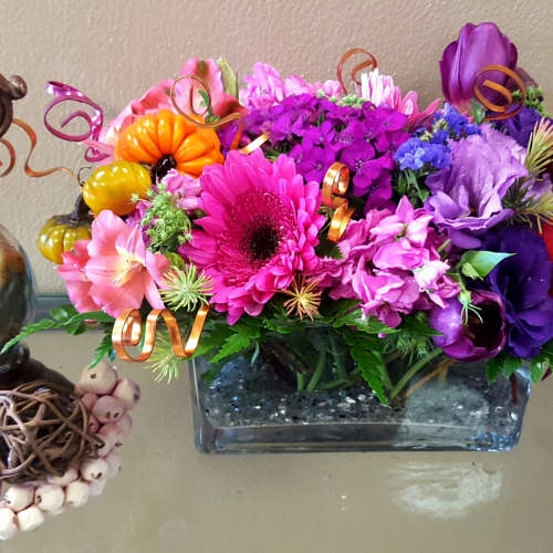 Bright mixed flower arrangement in a rectangular glass vase with decorative curls