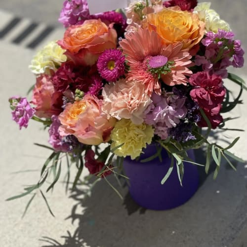 Mixed bouquet of roses, gerbera daisies, and carnations in a purple vase