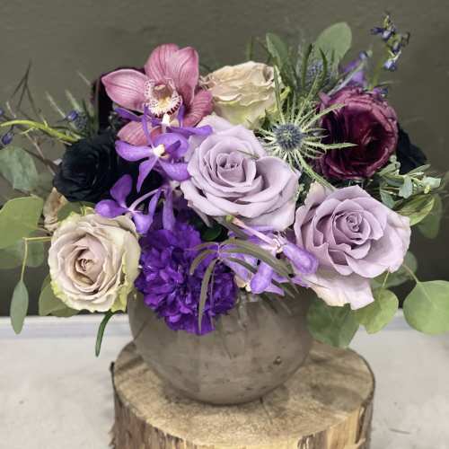 Purple and cream roses with orchids in a round vase