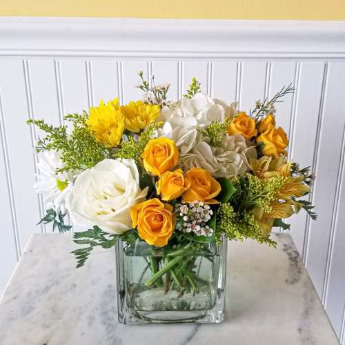 Yellow and white flower arrangement in a square glass vase