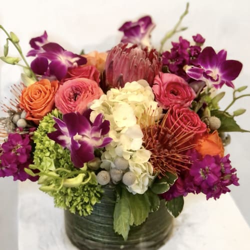 Mixed bouquet in a dark round vase with purple orchids and pink, orange, and white blooms