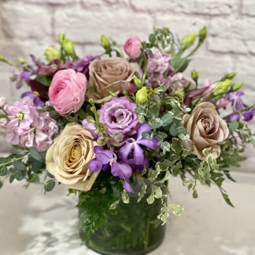 Mixed pink, purple, and beige flowers in a glass vase