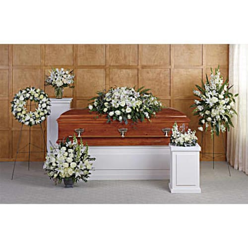 White funeral casket surrounded by white floral sprays and wreaths