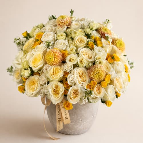 Cream and yellow rose bouquet in a gray vase with a ribbon