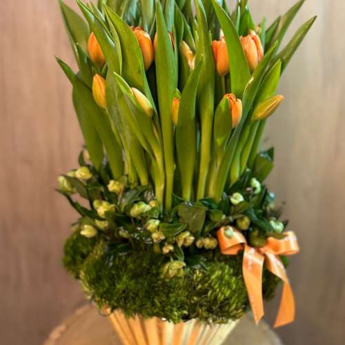 Orange tulips arranged in a gold vase with a ribbon