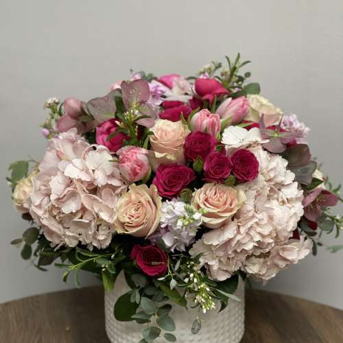 Low round arrangement of pink hydrangeas, roses, and tulips in a white ceramic vase