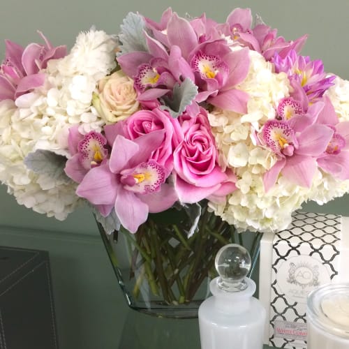 Pink orchids and roses arranged with white hydrangeas in a glass vase