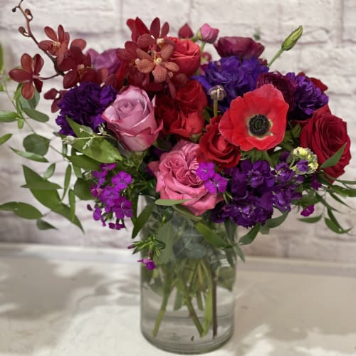 Mixed bouquet of red, pink, and purple flowers in a glass vase