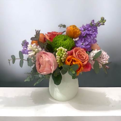 Mixed bouquet of roses, tulips, and purple stock in a white vase