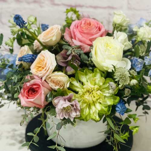 Mixed bouquet of pink, white, and blue flowers in a white vase