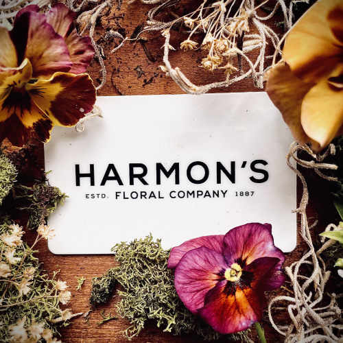 Pansies arranged around a Harmon's Floral Company card on a wooden surface.